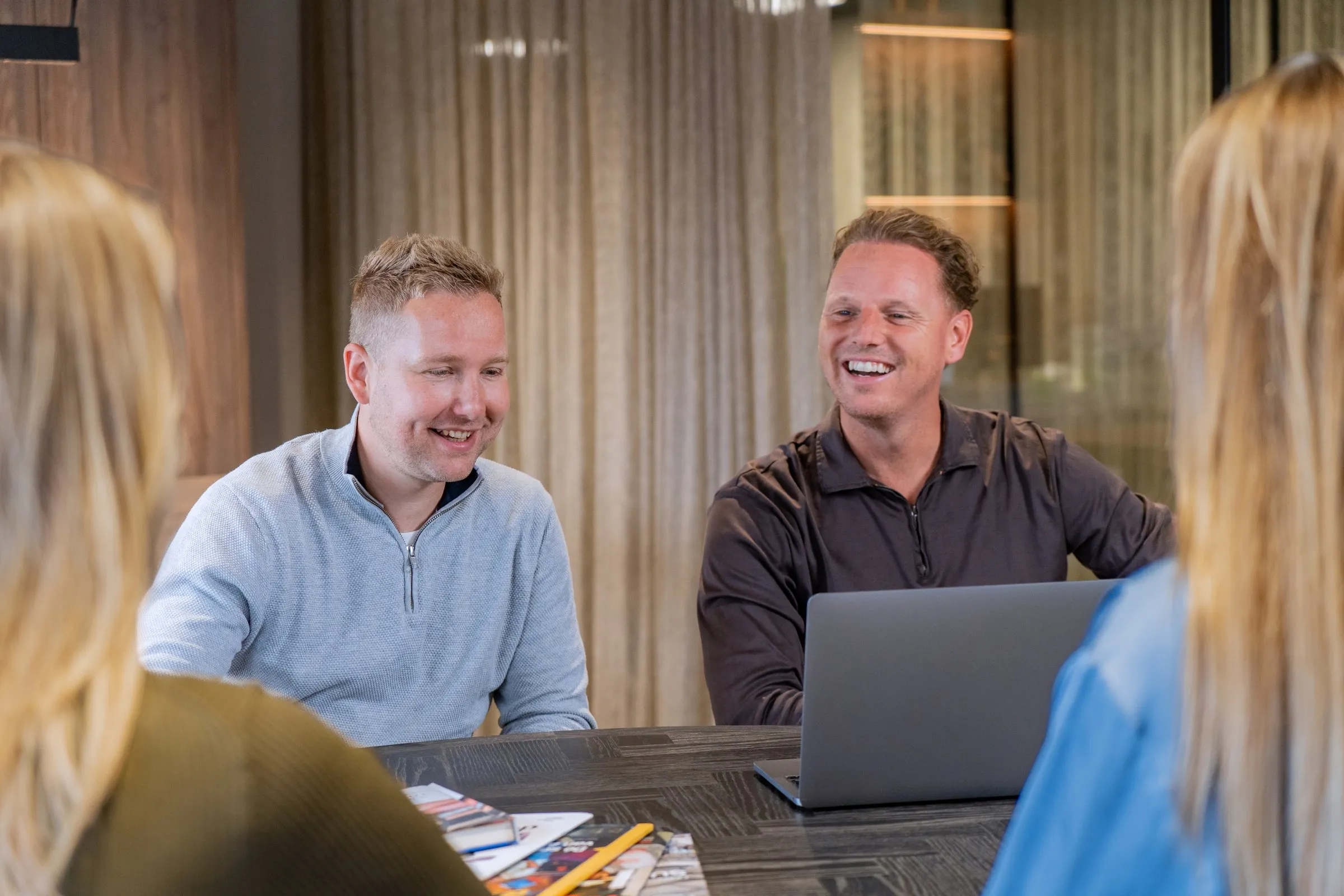 Daan Brinkkemper en Tim Bruin lachend aan tafel met klanten op het kantoor van De Groeispecialisten